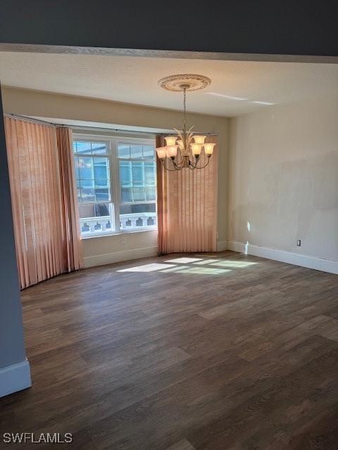 unfurnished dining area with baseboards, wood finished floors, and an inviting chandelier