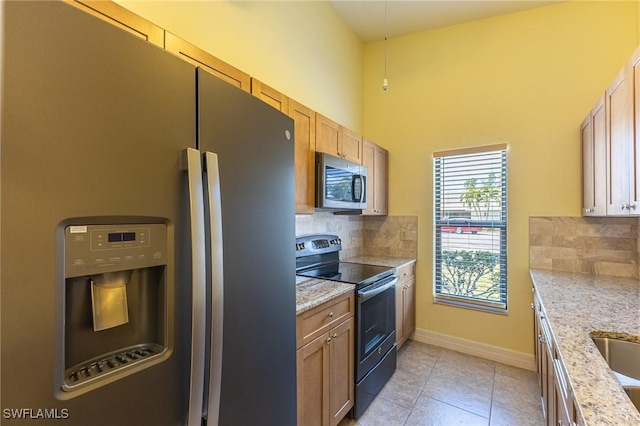 kitchen with light tile patterned floors, baseboards, decorative backsplash, appliances with stainless steel finishes, and light stone countertops