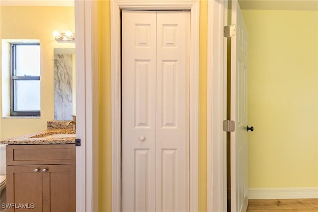 bathroom with a closet, toilet, vanity, wood finished floors, and baseboards