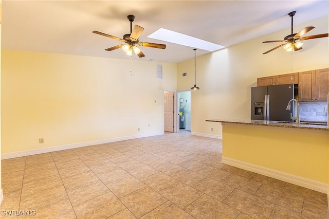 kitchen featuring a skylight, brown cabinets, ceiling fan, and stainless steel refrigerator with ice dispenser