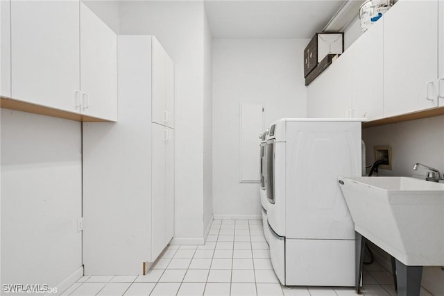 clothes washing area with cabinet space, washer / dryer, a sink, baseboards, and light tile patterned flooring
