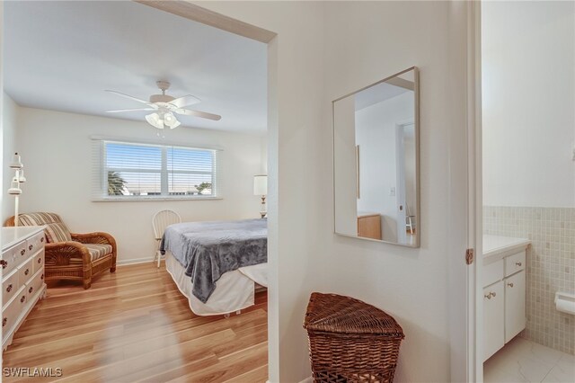 bedroom with light wood-style floors, ceiling fan, and tile walls