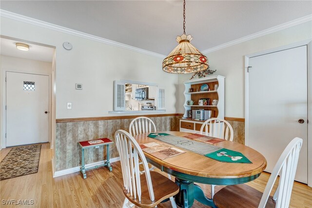 dining room with light wood finished floors, ornamental molding, and wainscoting