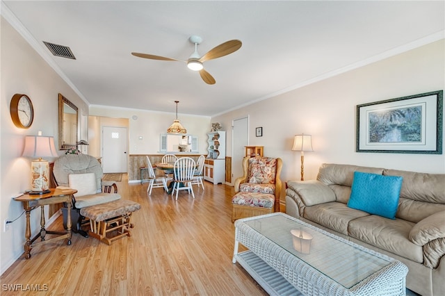 living area with ornamental molding, visible vents, light wood-style flooring, and a ceiling fan