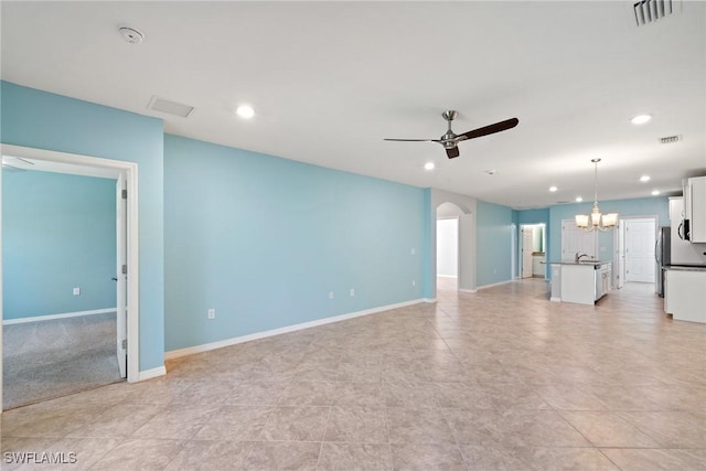 unfurnished living room featuring arched walkways, ceiling fan with notable chandelier, a sink, visible vents, and baseboards