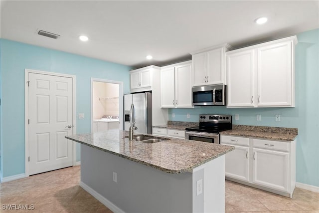 kitchen featuring a kitchen island with sink, stainless steel appliances, a sink, visible vents, and washer and clothes dryer