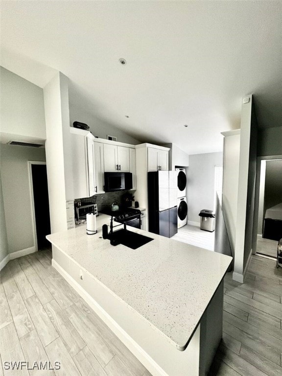 kitchen featuring a peninsula, a sink, black appliances, light wood finished floors, and stacked washer and clothes dryer