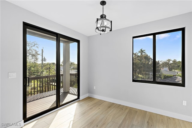 unfurnished room with a chandelier, light wood-type flooring, and baseboards