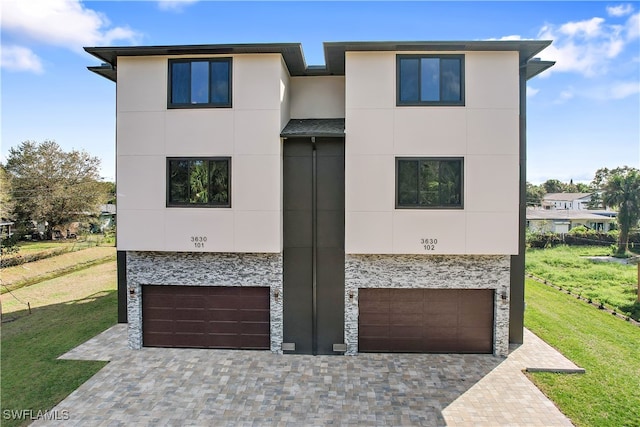 view of front of property featuring stone siding, a front lawn, an attached garage, and stucco siding