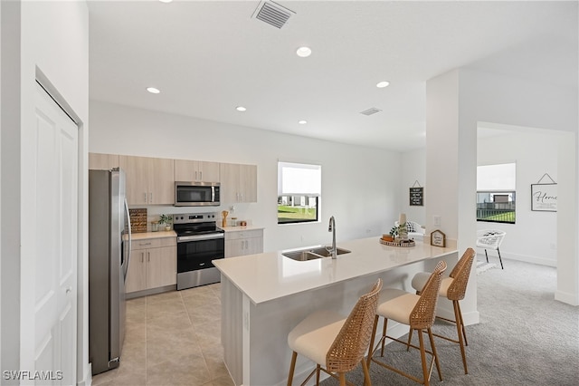 kitchen featuring a kitchen bar, light brown cabinetry, a sink, stainless steel appliances, and a peninsula