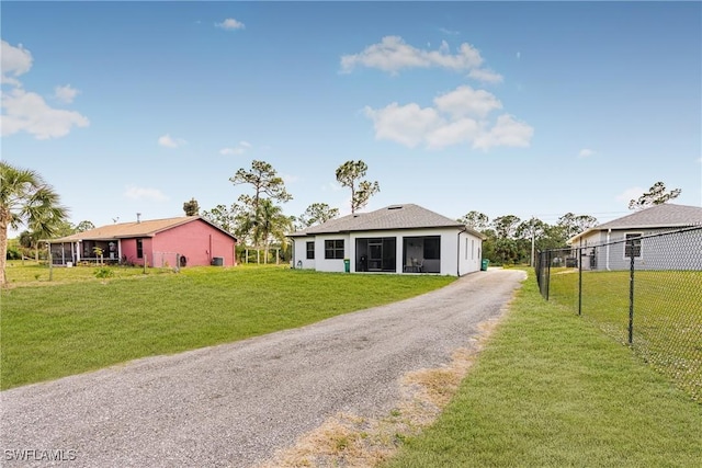 view of front of house featuring gravel driveway, a sunroom, fence, and a front lawn