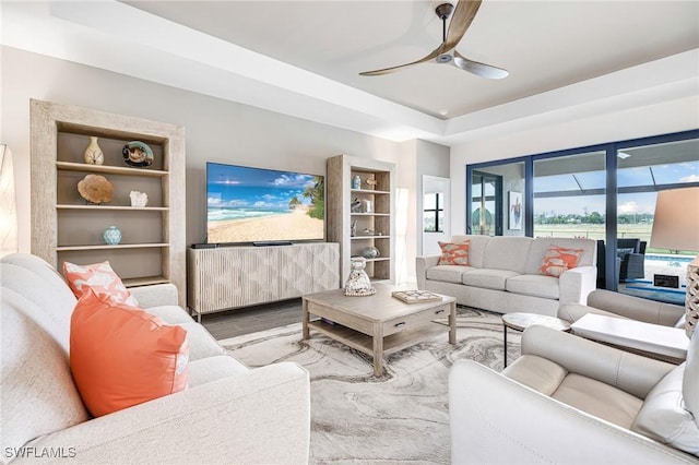 living room featuring a tray ceiling, built in shelves, a ceiling fan, and wood finished floors