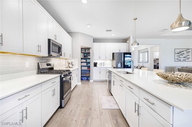 kitchen with appliances with stainless steel finishes, light countertops, a sink, and light wood finished floors