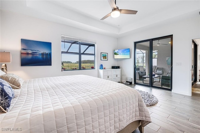 bedroom with access to exterior, a tray ceiling, light wood-style floors, ceiling fan, and baseboards