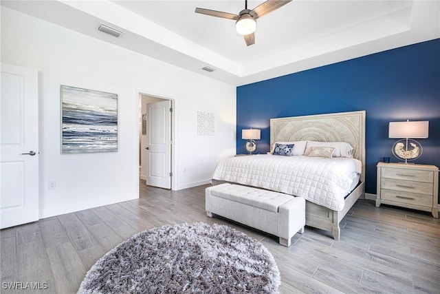 bedroom featuring baseboards, visible vents, a raised ceiling, ceiling fan, and wood finished floors