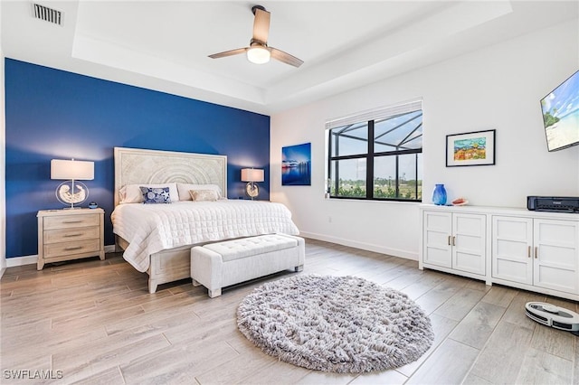 bedroom featuring light wood finished floors, visible vents, a tray ceiling, and baseboards