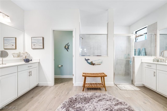 full bath with a stall shower, two vanities, wood finished floors, and baseboards