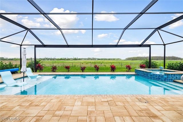 view of swimming pool featuring glass enclosure, a pool with connected hot tub, a patio area, and a rural view