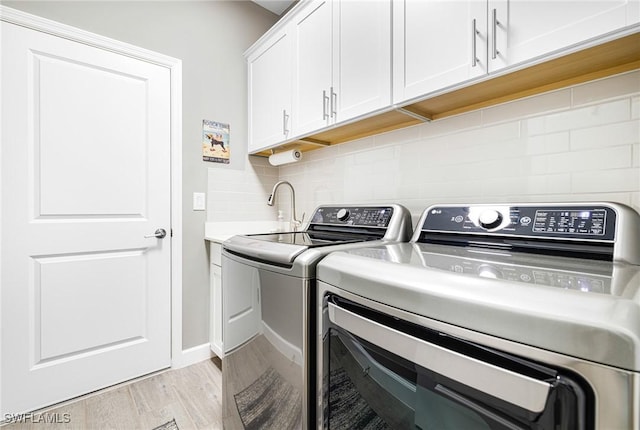 clothes washing area with cabinet space, light wood finished floors, a sink, and independent washer and dryer