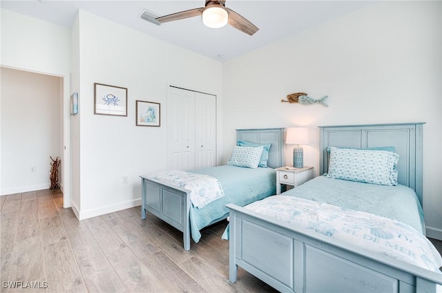 bedroom featuring visible vents, a ceiling fan, baseboards, a closet, and light wood finished floors