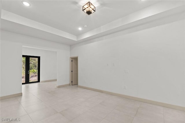 unfurnished room with a tray ceiling, recessed lighting, french doors, and baseboards