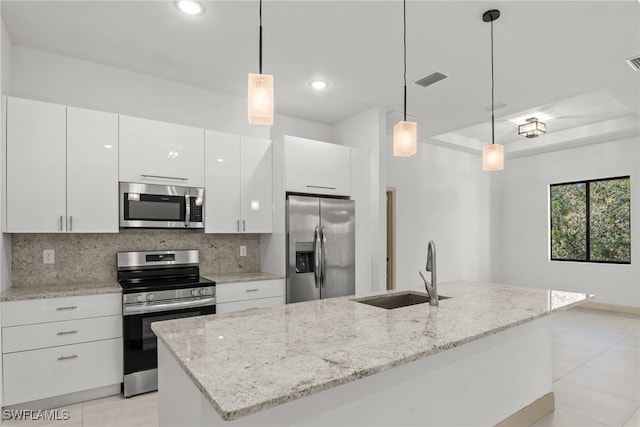 kitchen featuring a kitchen island with sink, a sink, tasteful backsplash, white cabinetry, and stainless steel appliances