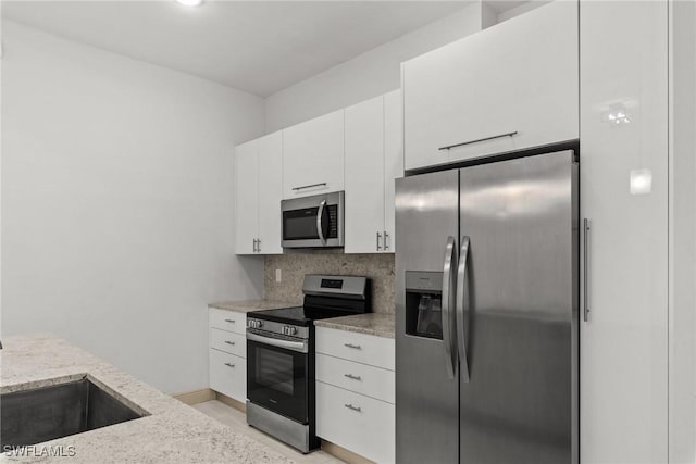 kitchen featuring tasteful backsplash, white cabinetry, stainless steel appliances, baseboards, and light stone countertops