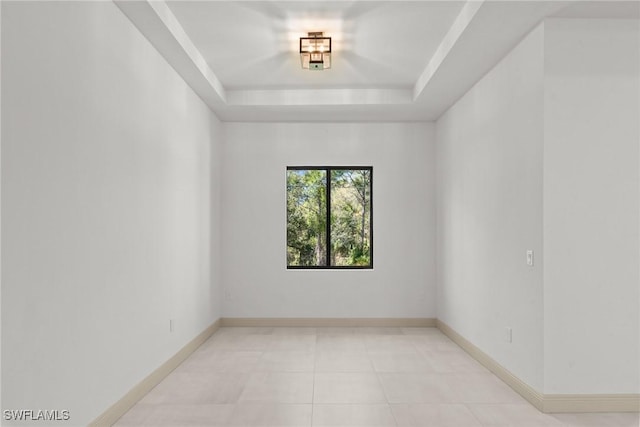 tiled spare room with a raised ceiling and baseboards