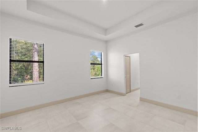 spare room featuring visible vents, a raised ceiling, and baseboards