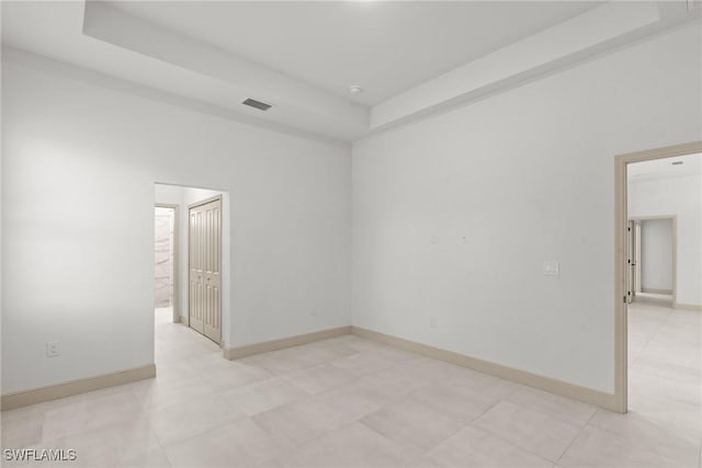 empty room featuring a raised ceiling, baseboards, and visible vents