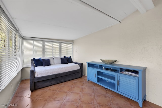 bedroom featuring a textured wall, beamed ceiling, and tile patterned flooring