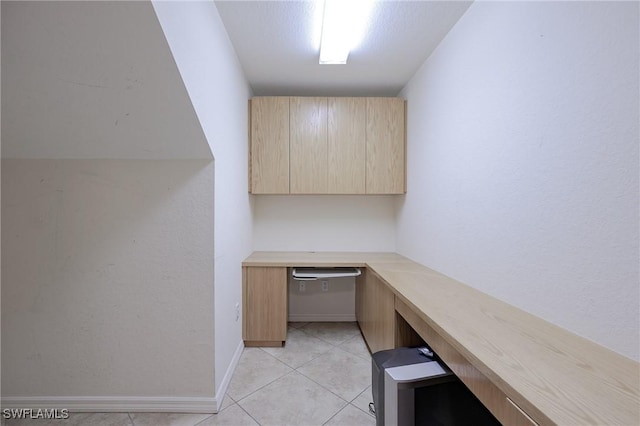 unfurnished office featuring built in desk, light tile patterned floors, and baseboards