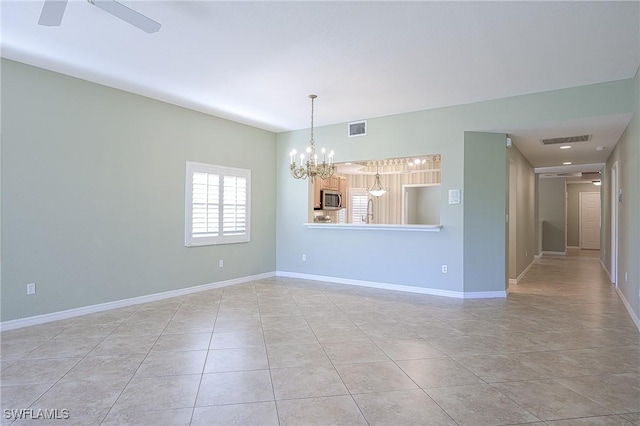 empty room featuring a chandelier, ceiling fan, light tile patterned floors, and baseboards