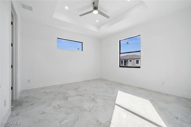 spare room featuring a ceiling fan, a wealth of natural light, a raised ceiling, and visible vents