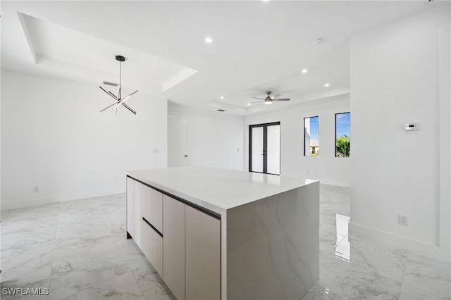 kitchen with a tray ceiling, a center island, marble finish floor, recessed lighting, and modern cabinets