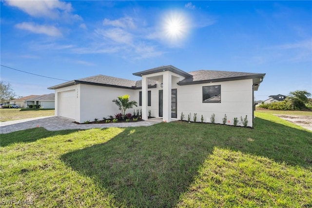 prairie-style home featuring a garage, roof with shingles, decorative driveway, and a front yard