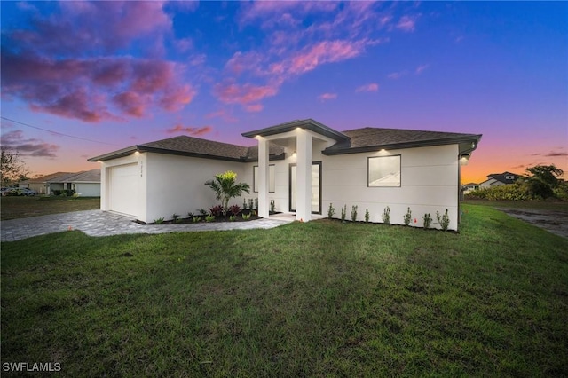 prairie-style home with a shingled roof, decorative driveway, a lawn, and an attached garage