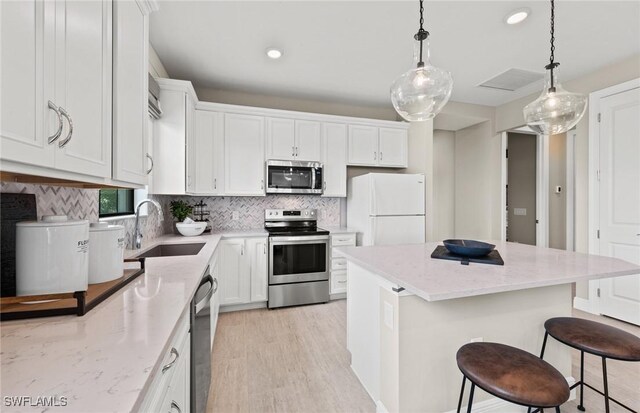 kitchen featuring light stone counters, stainless steel appliances, a sink, white cabinets, and tasteful backsplash