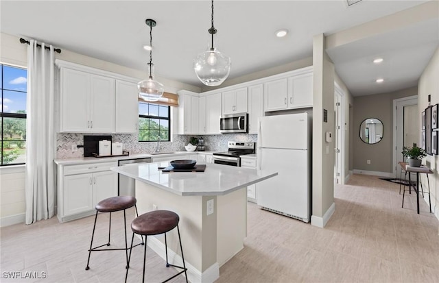 kitchen featuring decorative backsplash, appliances with stainless steel finishes, white cabinets, a kitchen island, and a kitchen breakfast bar