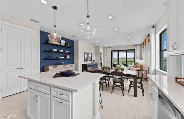 kitchen with visible vents, hanging light fixtures, stainless steel dishwasher, white cabinetry, and a kitchen island