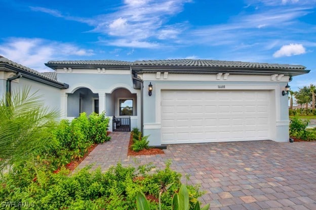 view of front of home featuring an attached garage, covered porch, a tile roof, decorative driveway, and stucco siding