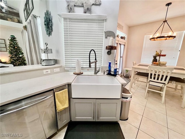 kitchen with light countertops, gray cabinetry, stainless steel dishwasher, a sink, and light tile patterned flooring