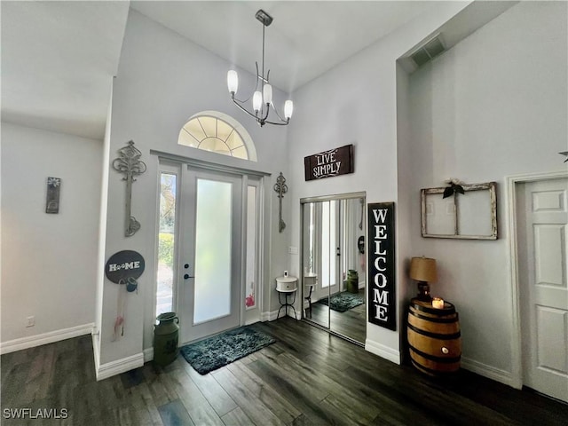 entryway with dark wood-style flooring, visible vents, a towering ceiling, an inviting chandelier, and baseboards