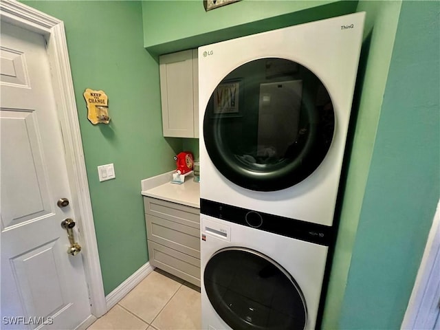 laundry room featuring light tile patterned floors, stacked washer and dryer, cabinet space, and baseboards