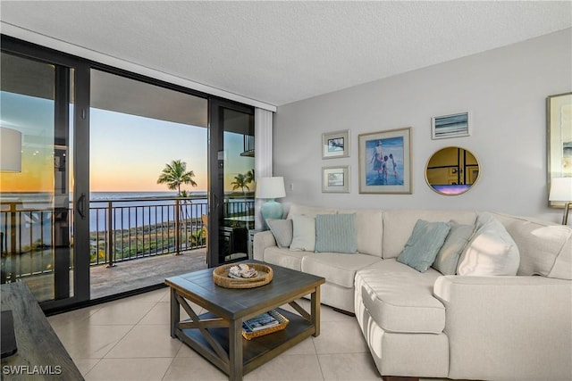 living area with expansive windows, light tile patterned floors, a textured ceiling, and a water view