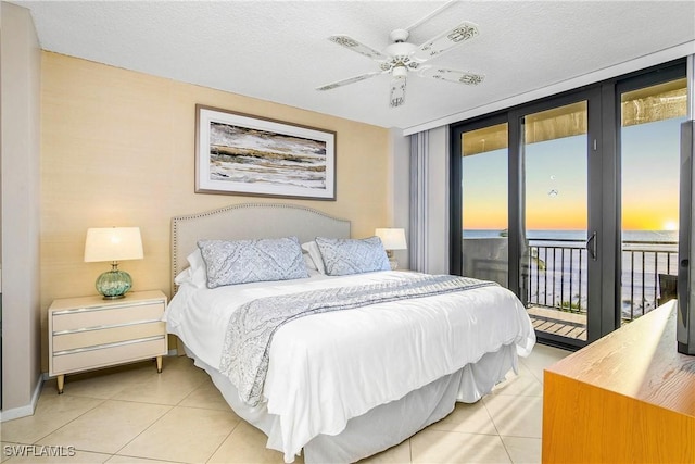 bedroom featuring access to exterior, light tile patterned floors, a water view, expansive windows, and a textured ceiling