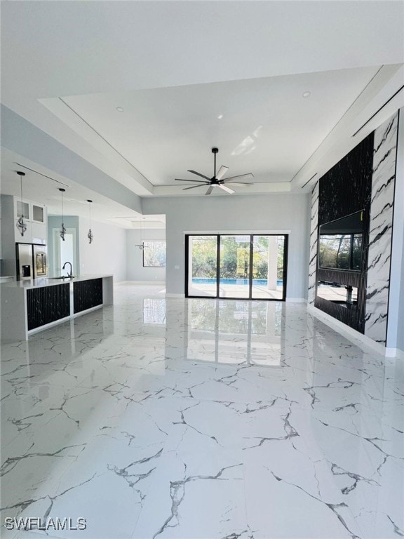 unfurnished living room featuring ceiling fan, marble finish floor, and a tray ceiling