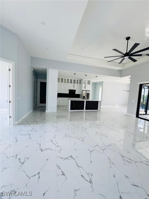 unfurnished living room featuring baseboards, a ceiling fan, marble finish floor, a tray ceiling, and recessed lighting