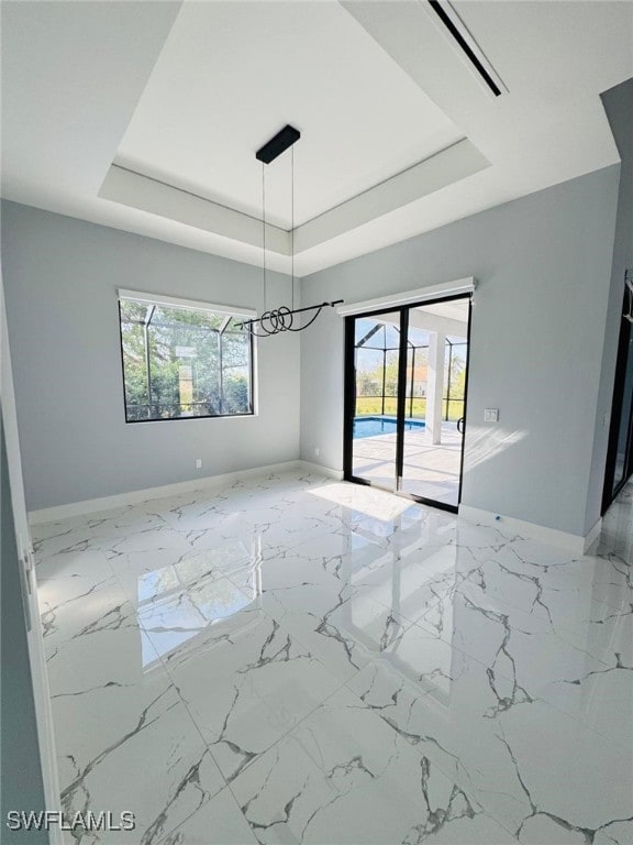 empty room featuring a raised ceiling, marble finish floor, and baseboards