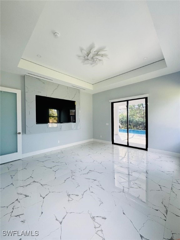 unfurnished living room featuring marble finish floor, baseboards, and a raised ceiling